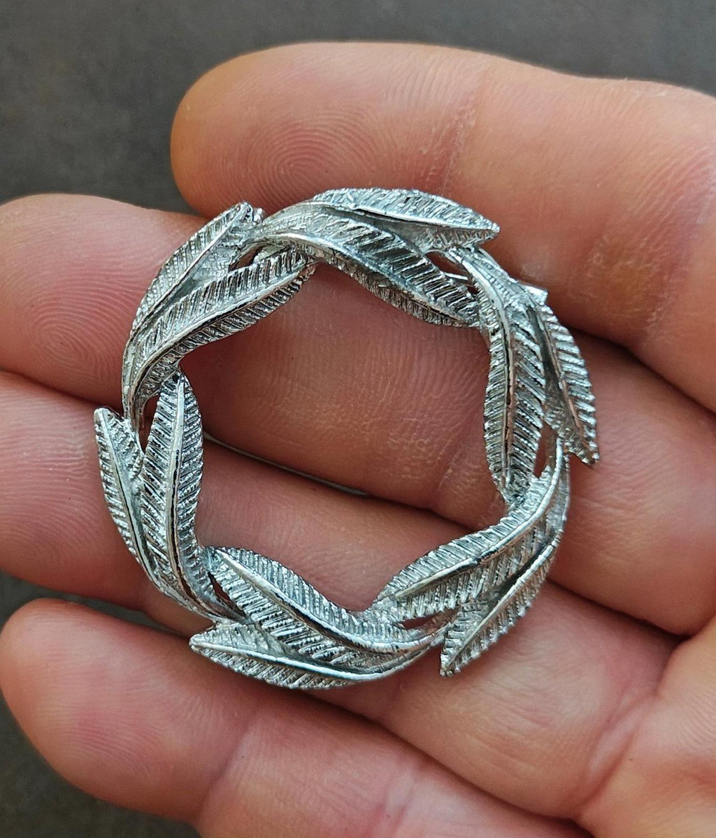 Silver-tone circular leaf textured pin brooch, open center held in hand