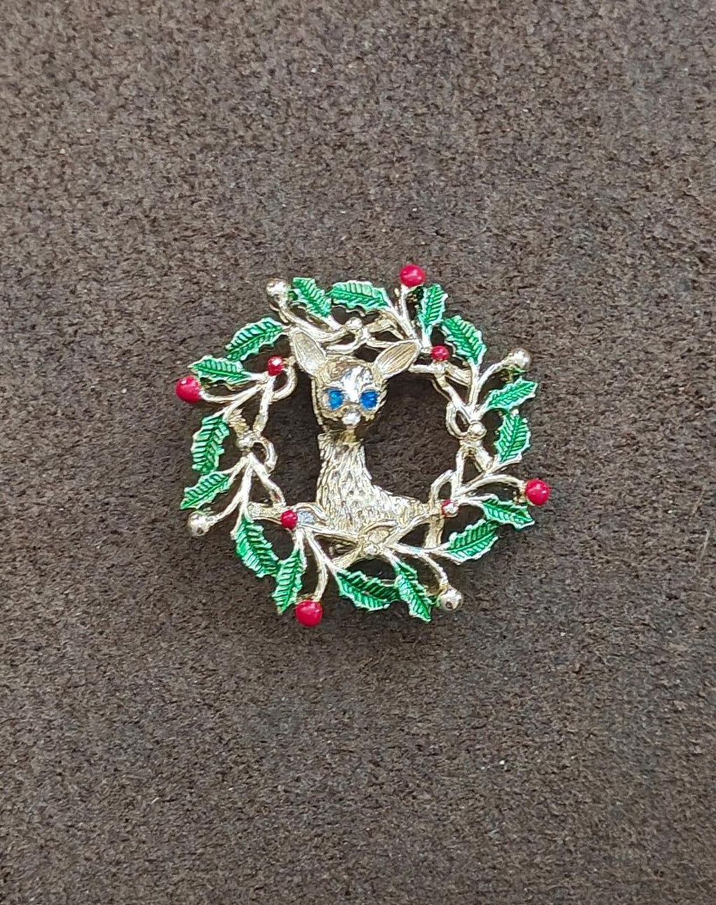 Enamel reindeer wreath brooch with green holly leaves, red berries, and blue face center