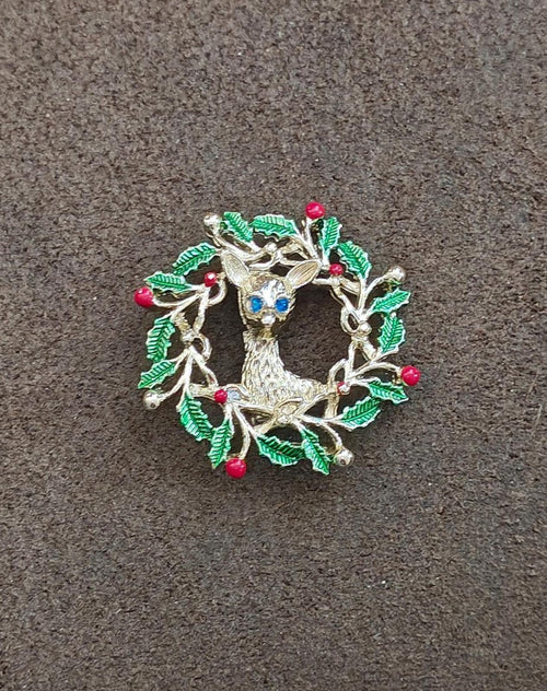 Enamel reindeer wreath brooch with green holly leaves, red berries, and blue face center