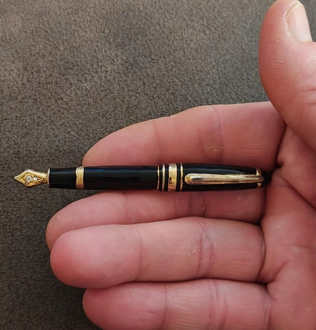 Black enamel fountain pen brooch with gold-tone accents and clear rhinestone tip detail.