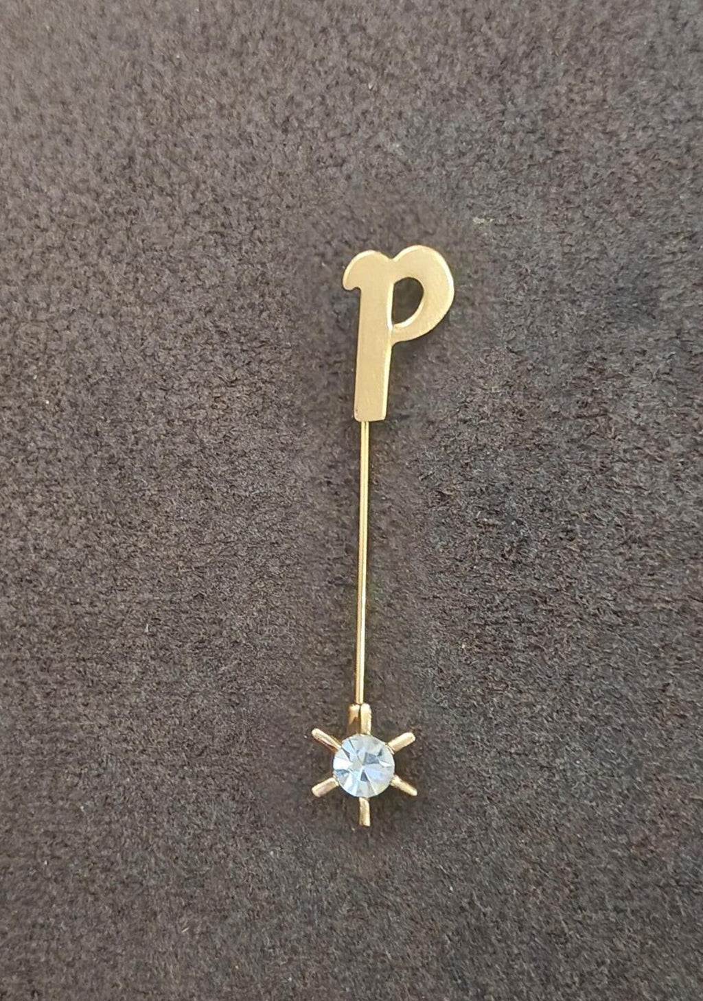 Gold tone P stick pin with round blue crystal head and pronged starburst base.