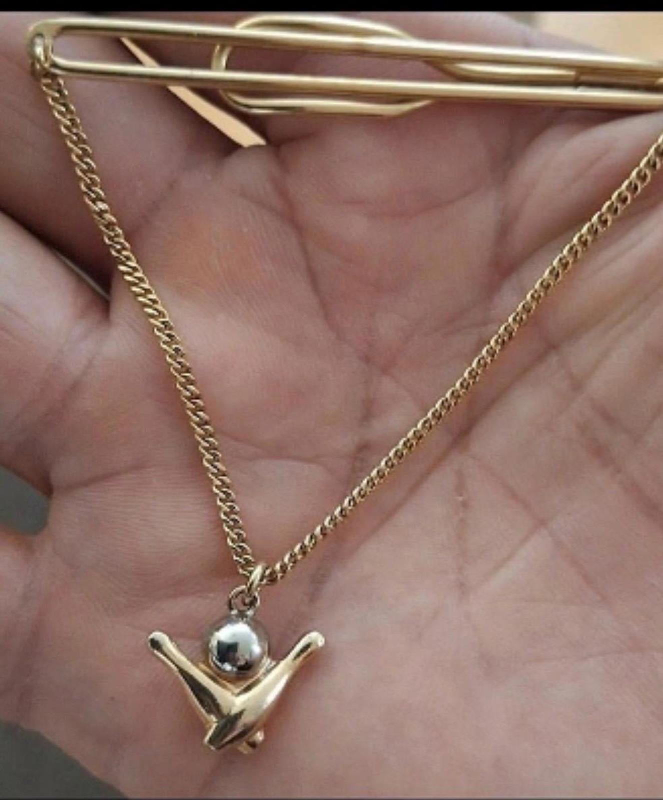 Bowling pin charm pendant on gold-tone chain, held above an open palm.
