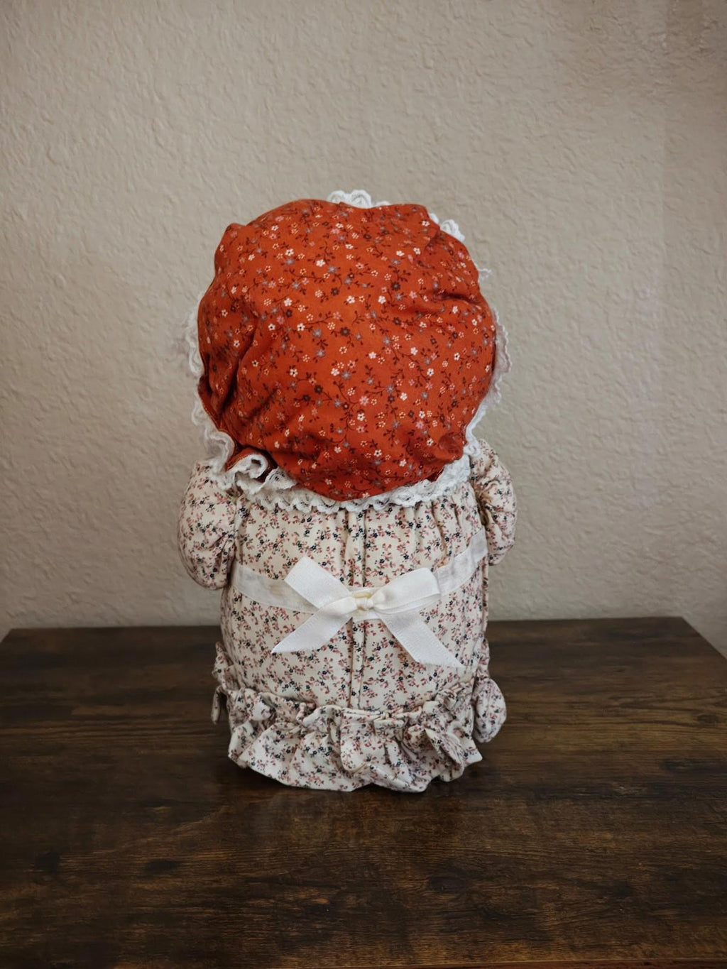Handmade cloth doll canister back view with red bonnet and white floral fabric dress.