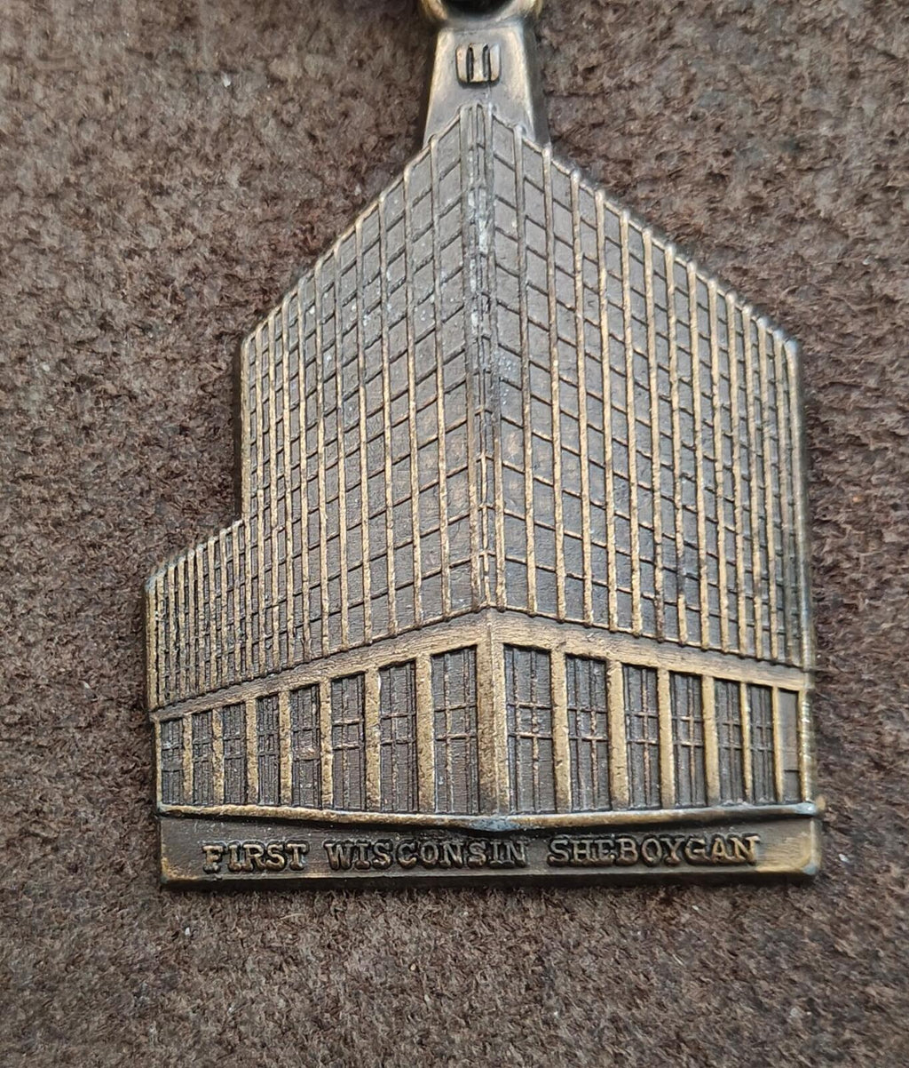 Metal building keychain charm in close-up with engraved base wording