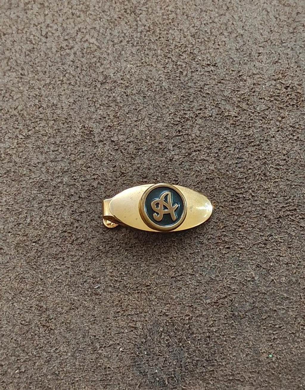 Gold-tone tie clip with blue-black circular monogram emblem on front
