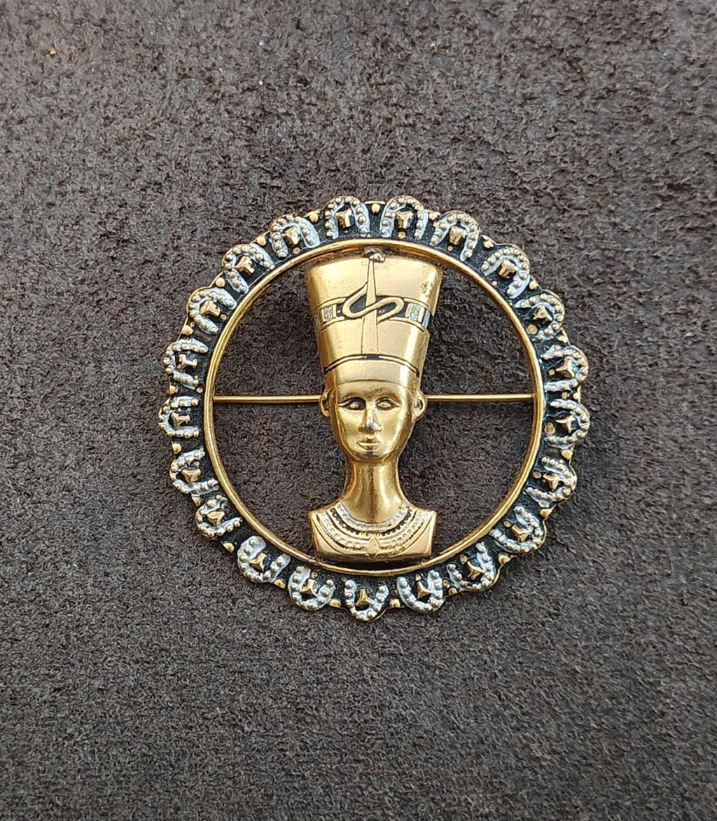 Gold-tone round brooch with Nefertiti profile medallion and blue rhinestone scalloped edge