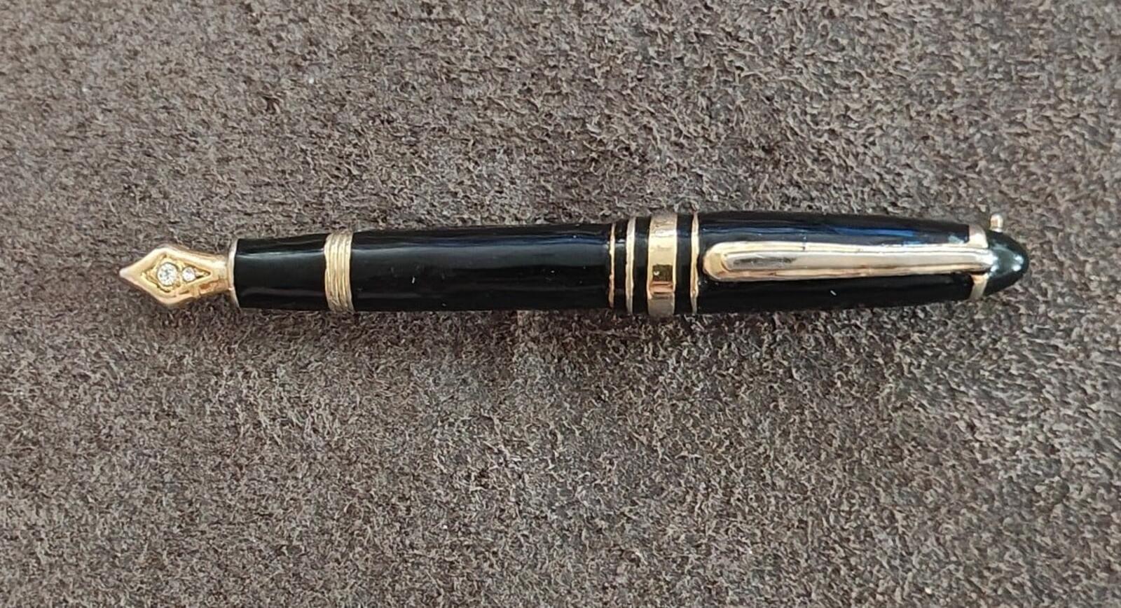 Black fountain pen brooch with gold-tone trim and clear rhinestone tip, side view.
