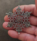 Silver tone snowflake filigree brooch with clear rhinestone accents, held in hand