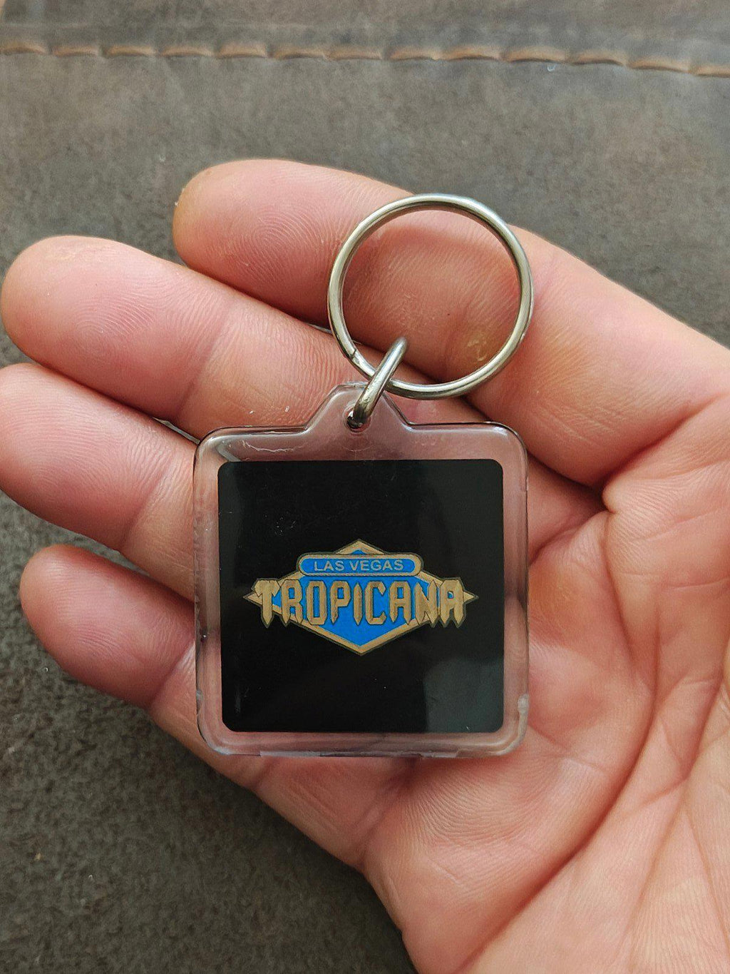 Square Tropicana logo keychain badge with metal ring in hand close-up