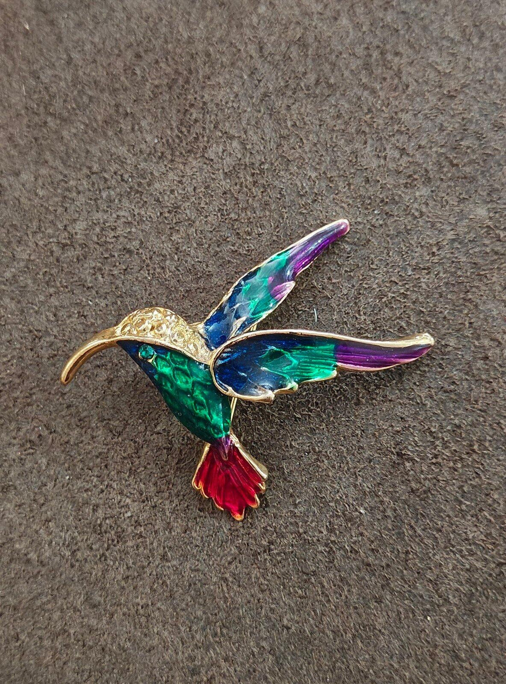 Gold tone hummingbird enamel pin with multicolor wings: green, blue, purple, red