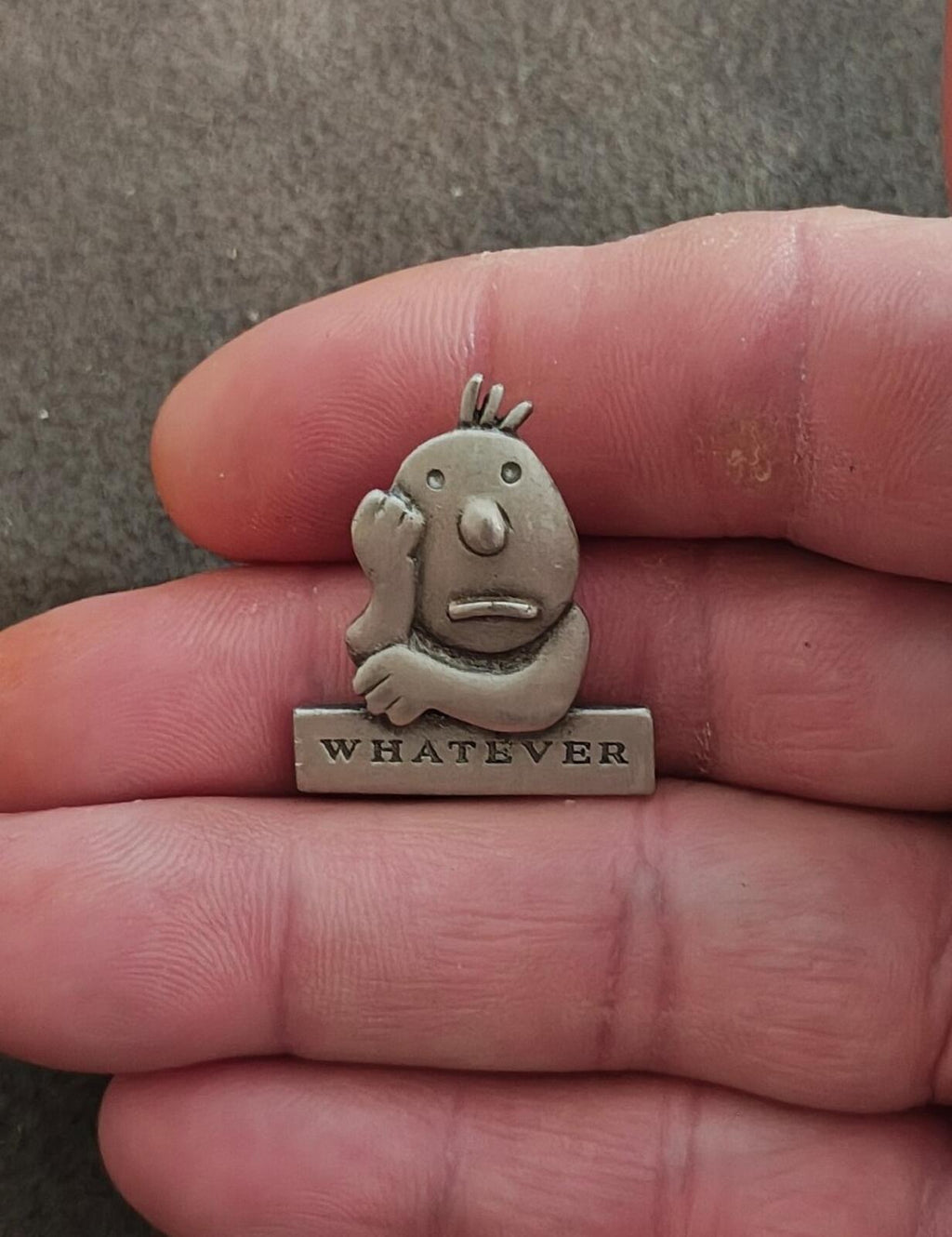 Vintage pewter cartoon pin on a hand, smiling character with raised hair, "WHATEVER" base
