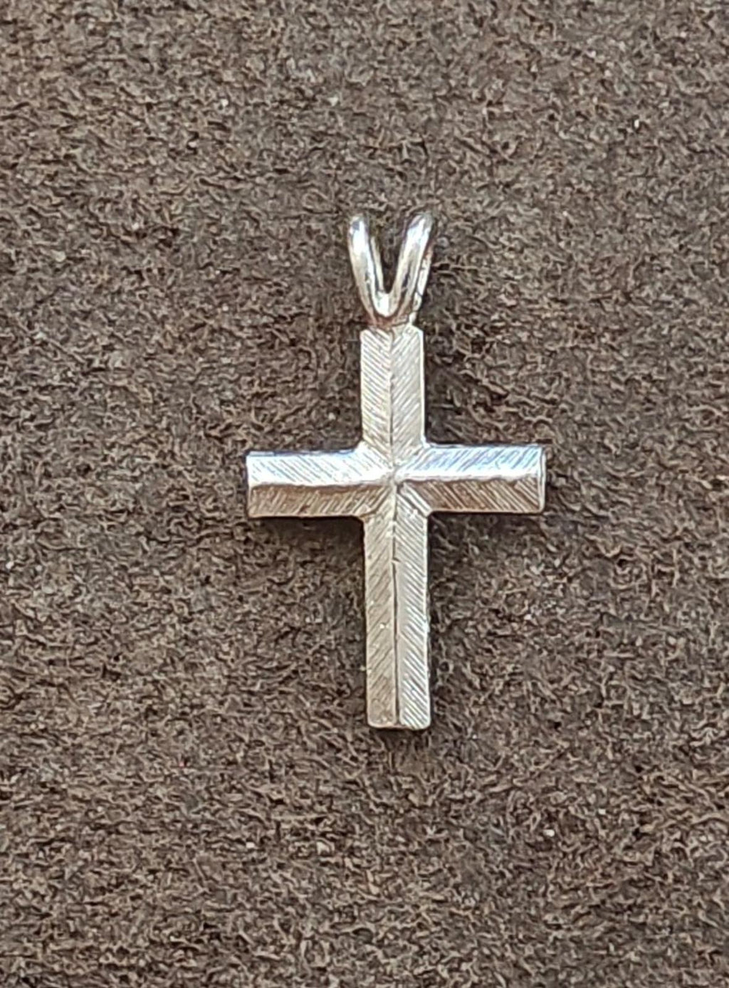 Silver tone cross pendant with engraved texture and pointed bail, no stones visible.