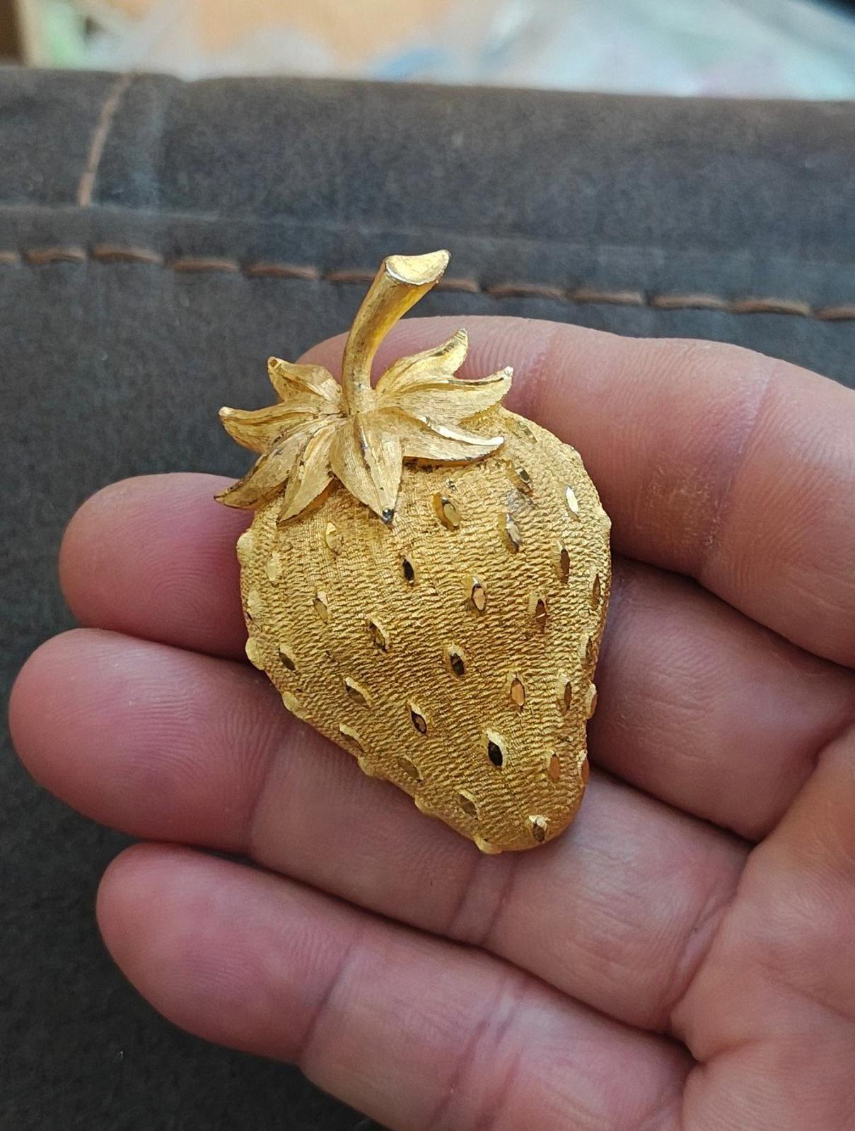 Gold tone strawberry brooch pin with stem and leaf cluster, textured seed dots.