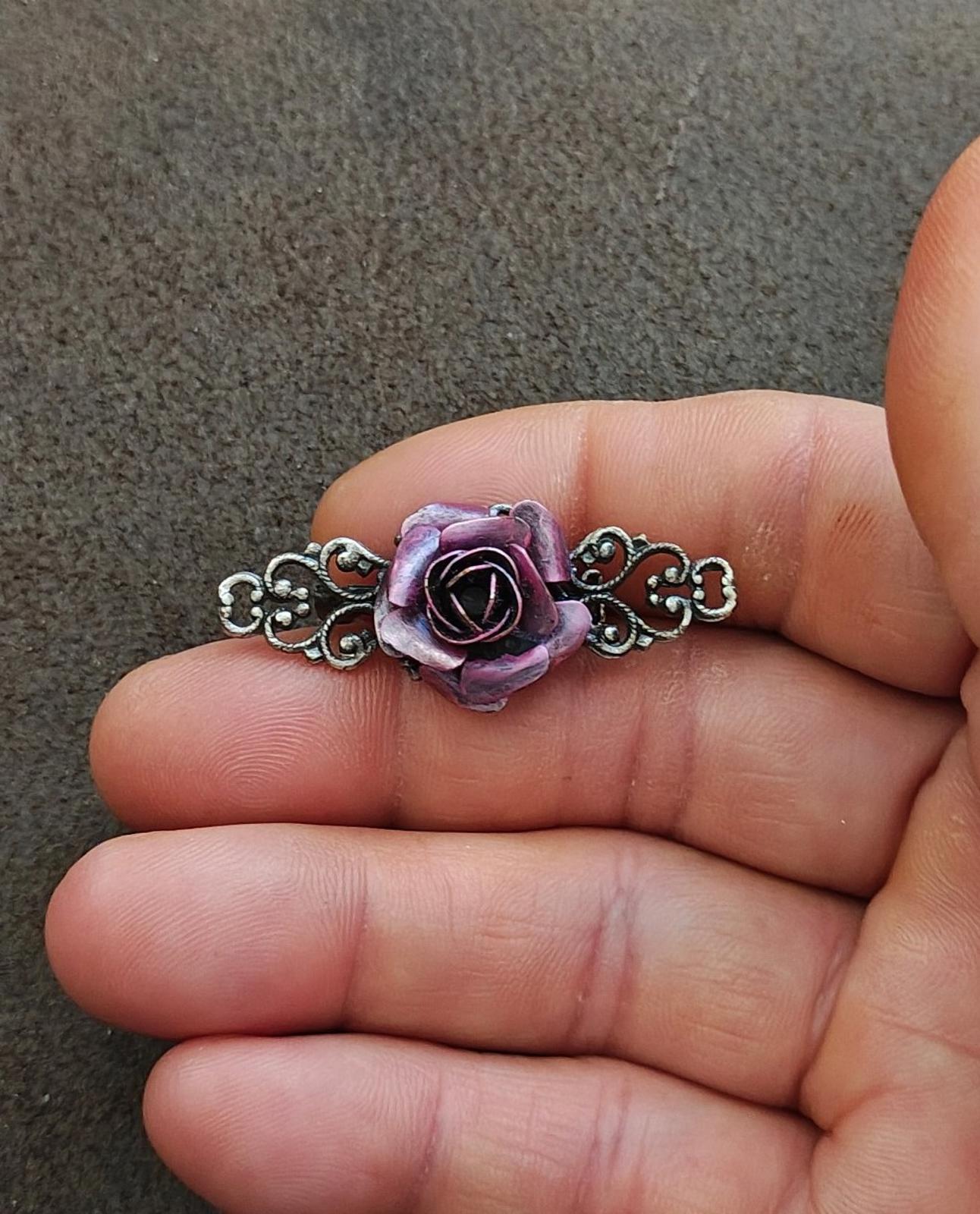 Purple rose and silver tone filigree brooch, close-up on fingertips