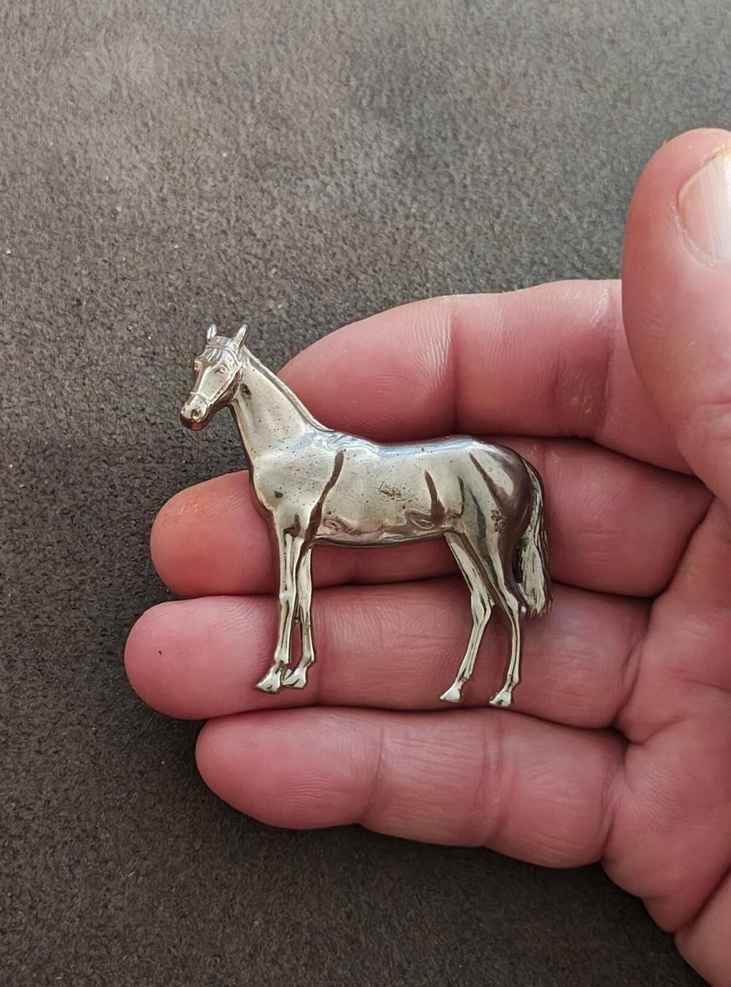 Silver-tone horse brooch with standing horse figure, close-up on hand