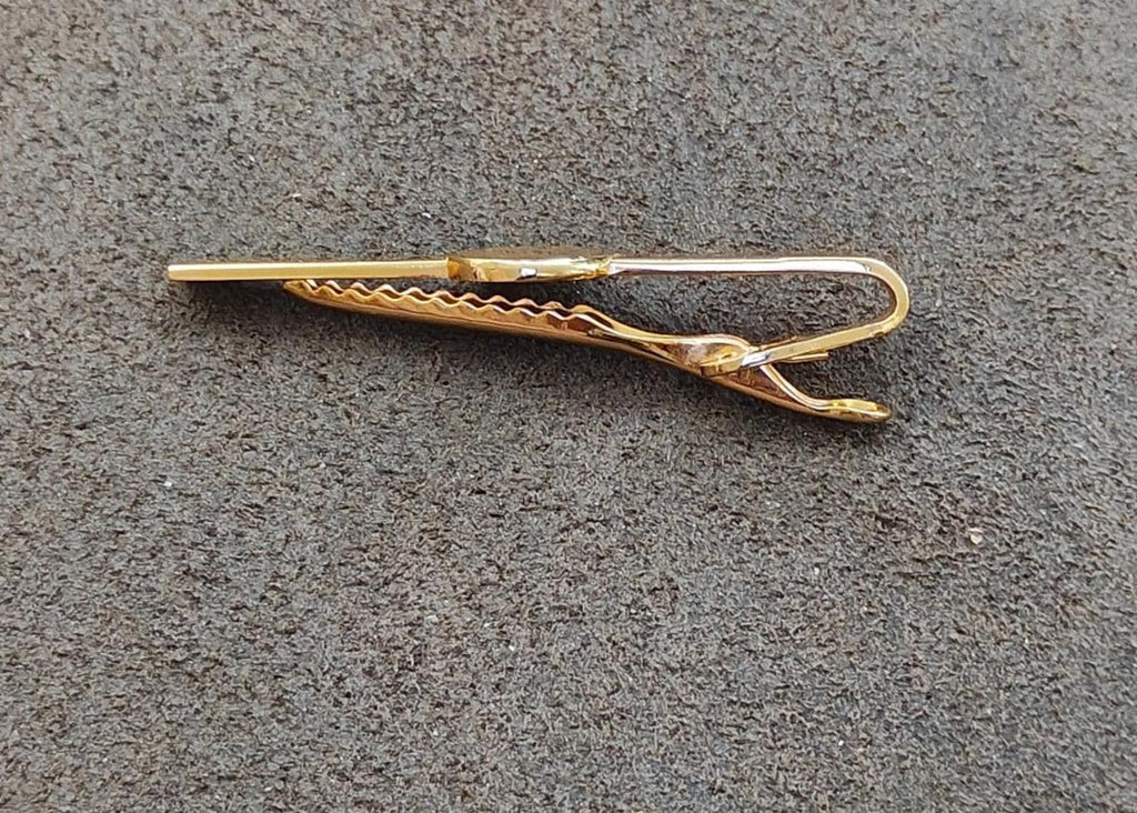 Gold-tone tie clip with angled prongs and textured grip detail