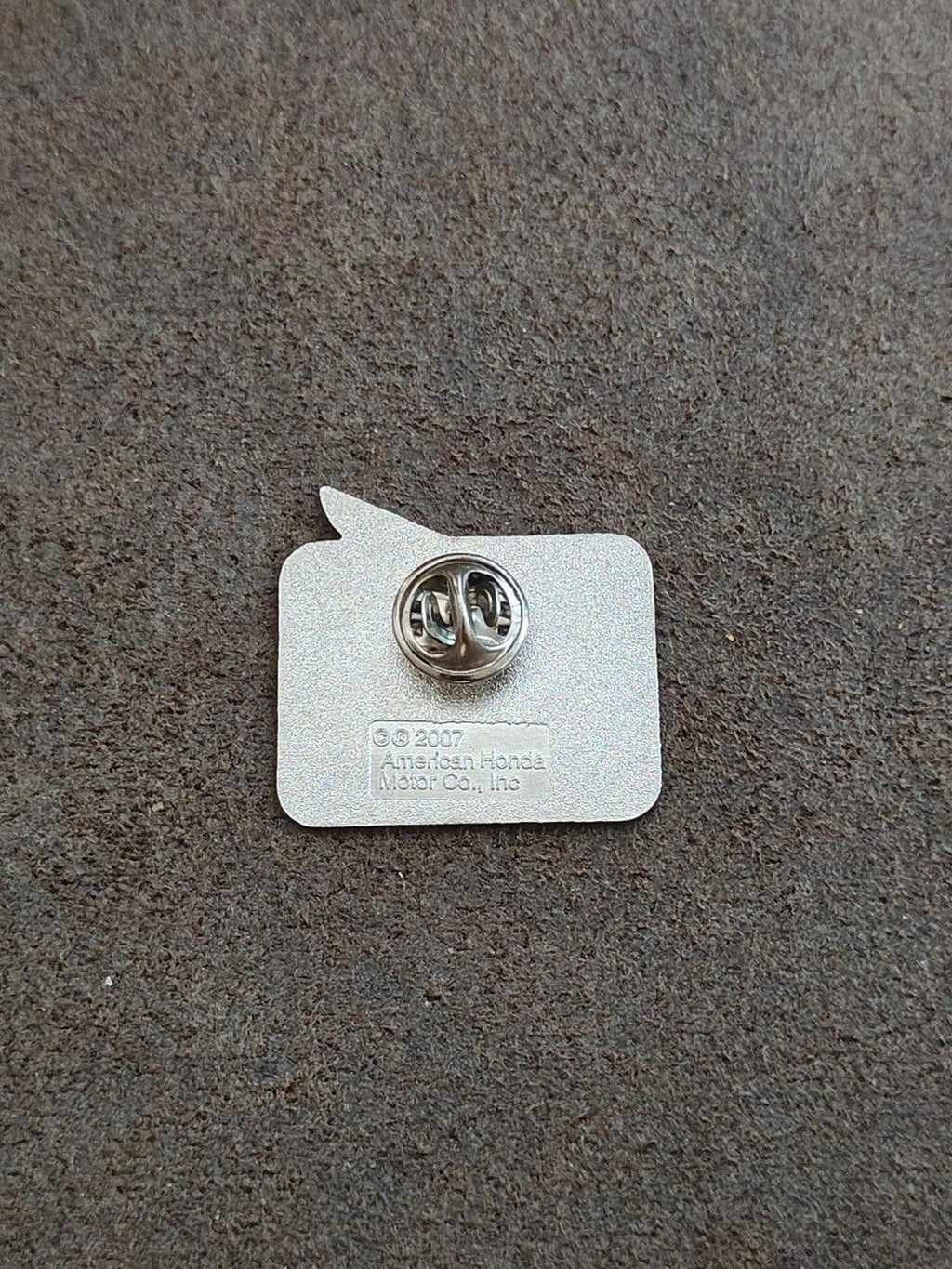 Back of silver-tone enamel pin with round metal clasp and maker markings