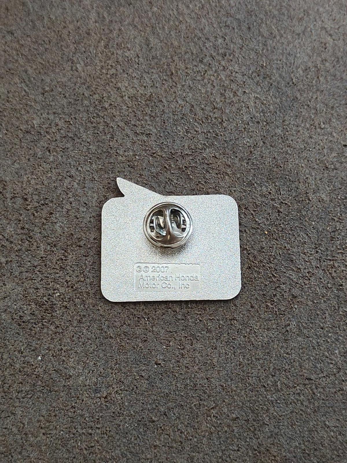 Back of silver-tone enamel pin with round metal clasp and maker markings