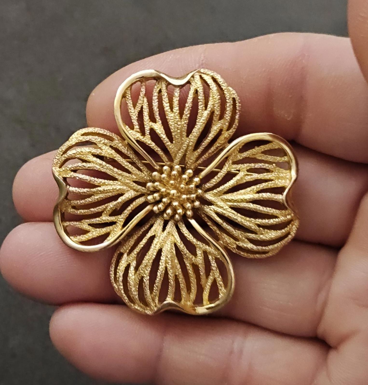 Gold-tone textured dogwood flower brooch with beaded center, held in hand