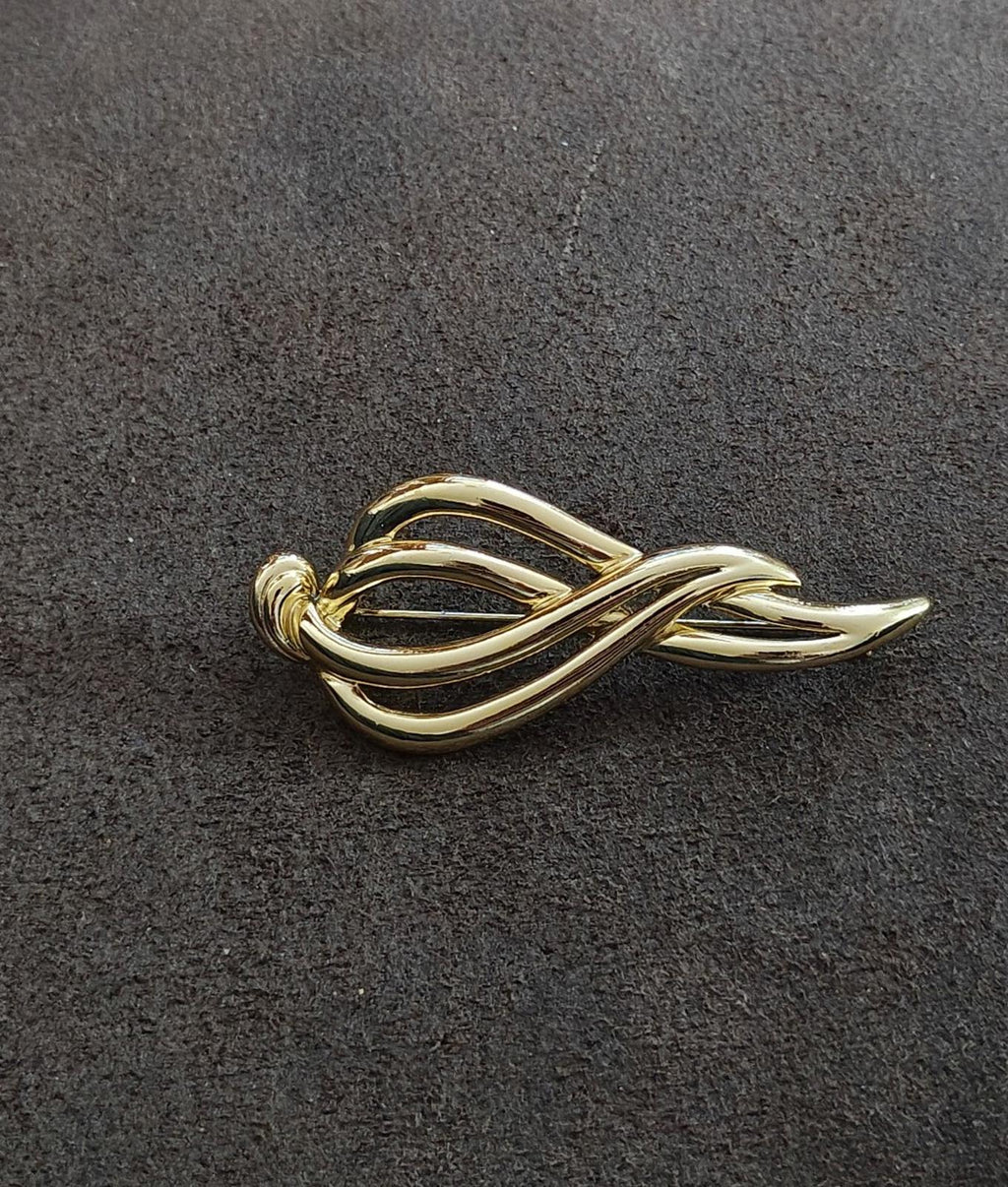 Gold-tone abstract ribbon-loop brooch with curved ovals, viewed from above.