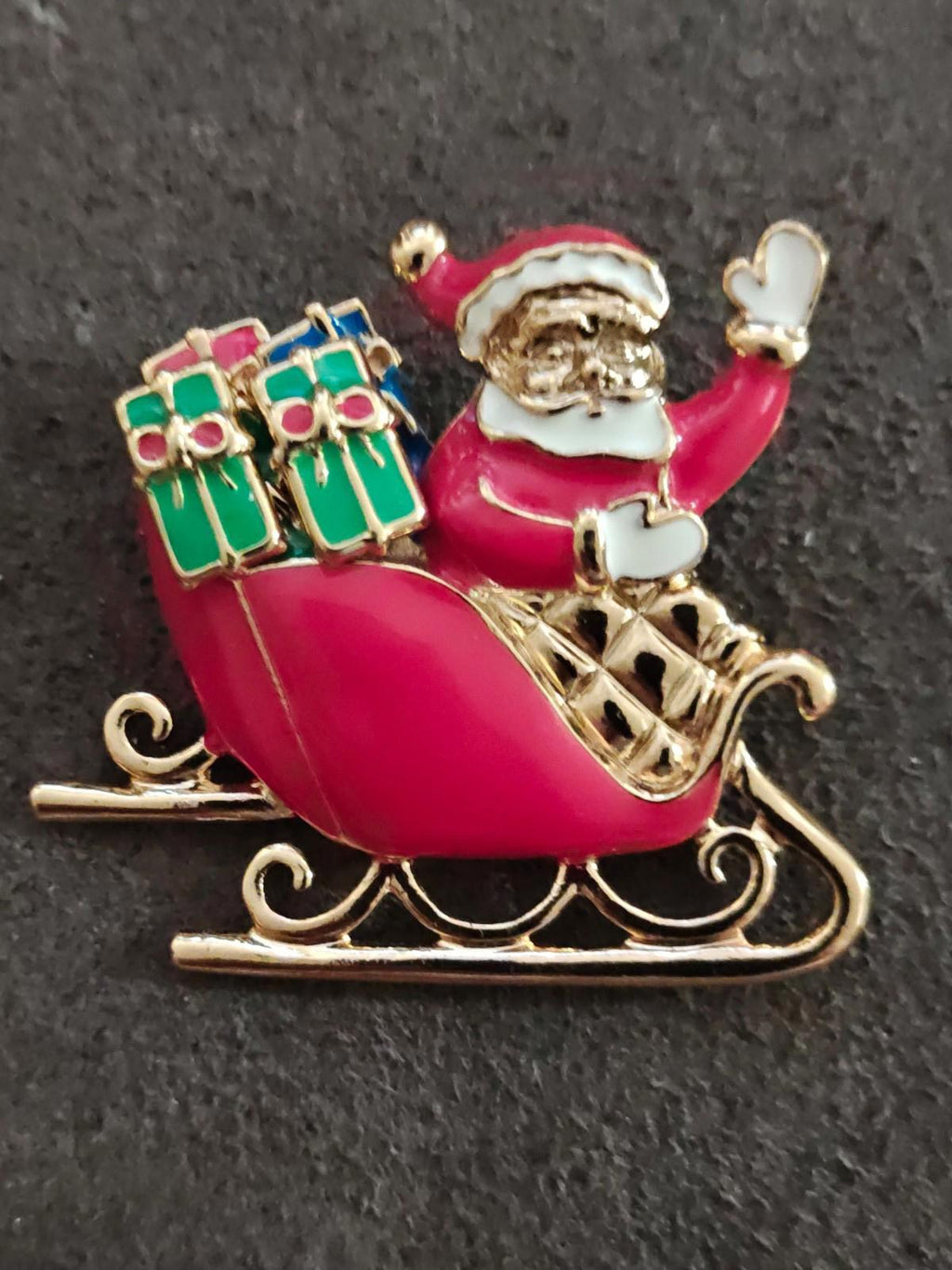 Close view of gold-tone Santa sleigh brooch with red enamel runner scroll base