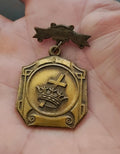 Gold award medal pin with round emblem, cross and crown inside engraved badge.