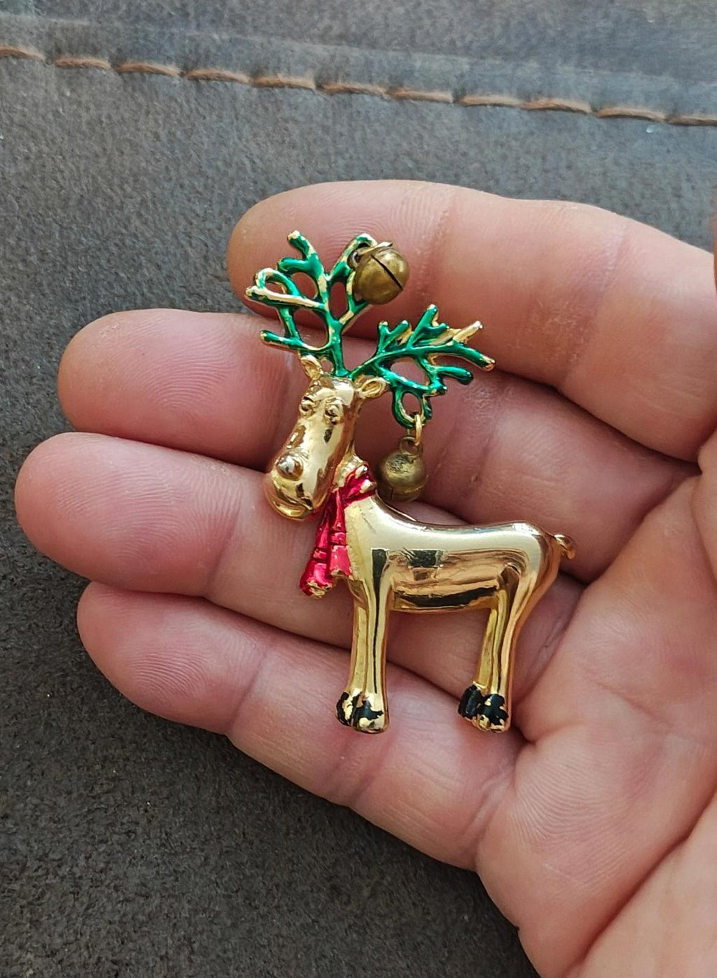 Gold-tone reindeer pin brooch in hand, green antlers with bells and red scarf.