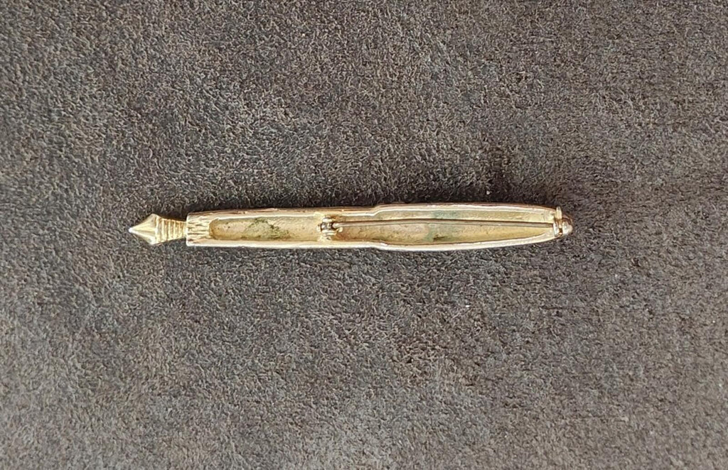 Gold-tone fountain pen brooch with pointed tip and clear rhinestone detail.