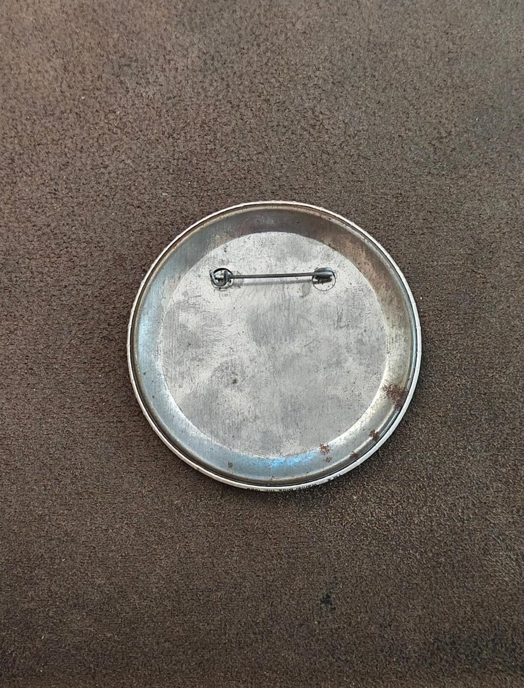 Metal back of round button pin with two-post pin clasp and worn silver finish.