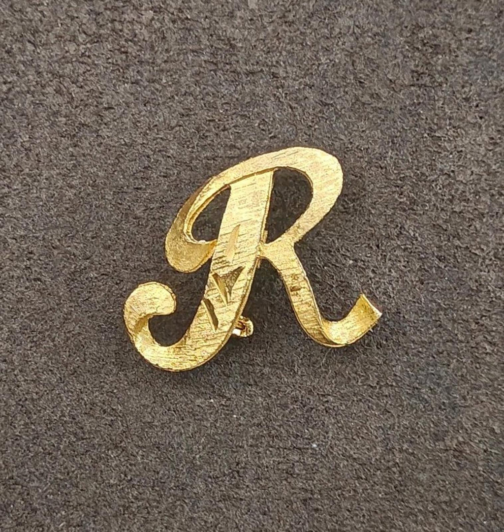 Gold tone monogram brooch pin featuring letter R, centered view