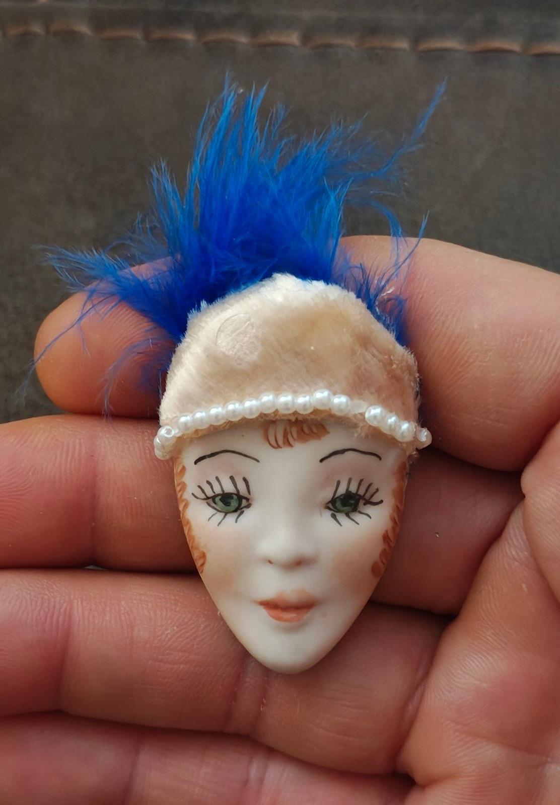 Doll face pin brooch with blue feather, cream headband, and faux pearl trim