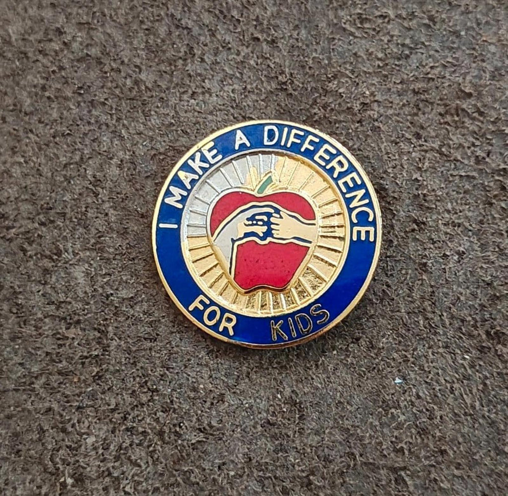 Round teacher pin with blue outer ring, gold spokes, and apple graphic enamel.
