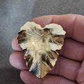 Gold-tone leaf scarf clip with textured veins and hinged design, held in hand
