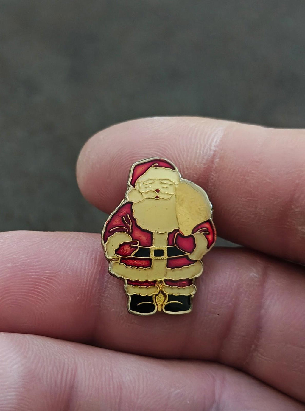 Red Santa Claus enamel pin, gold-tone outline, front view held between fingers