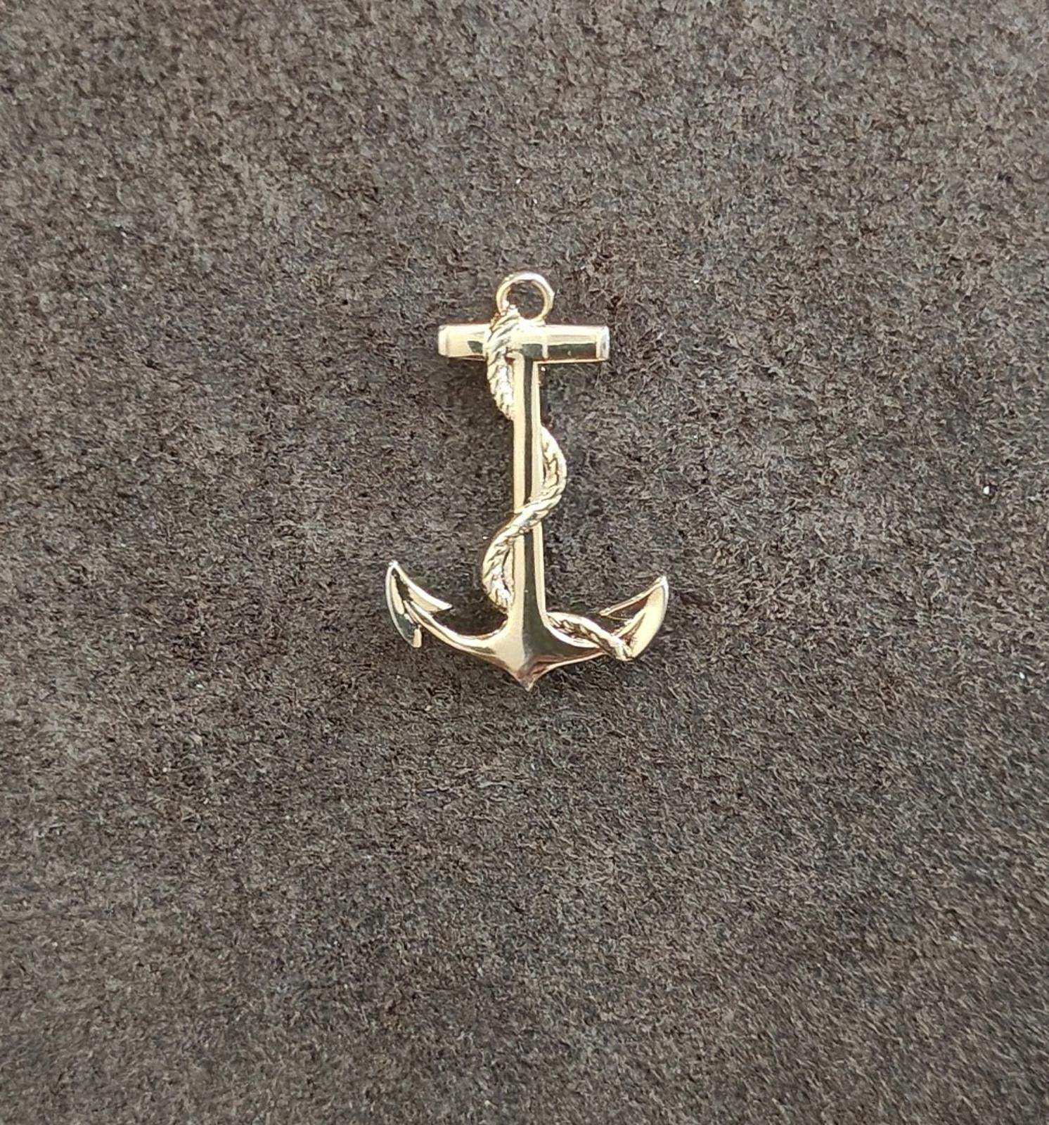 Gold-tone anchor pendant on textured surface, centered front view with loop