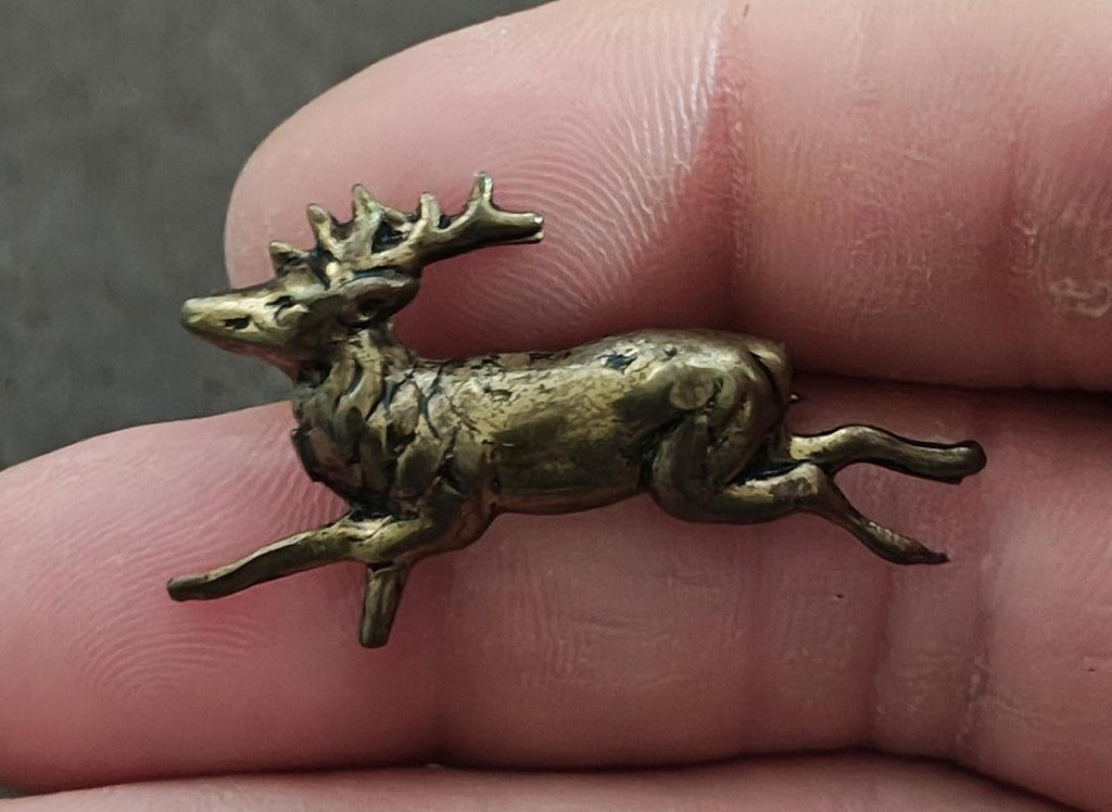 Brass leaping deer figurine with long antlers, raised legs, close-up on fingertip