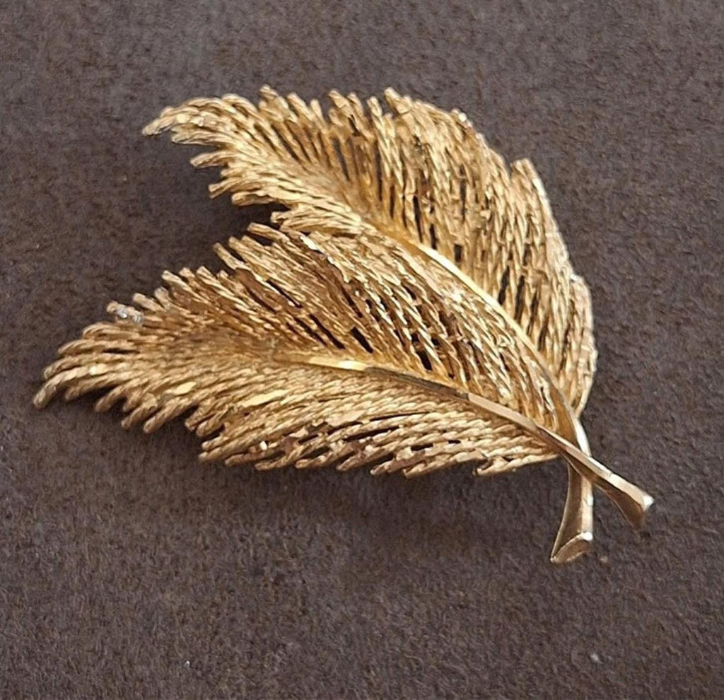 Gold-tone feather leaf brooch with layered texture and central vein, shown flat