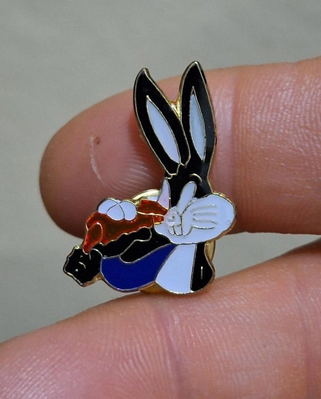 Enamel pin of Bugs Bunny holding a carrot, black ears, white face, blue body, orange details