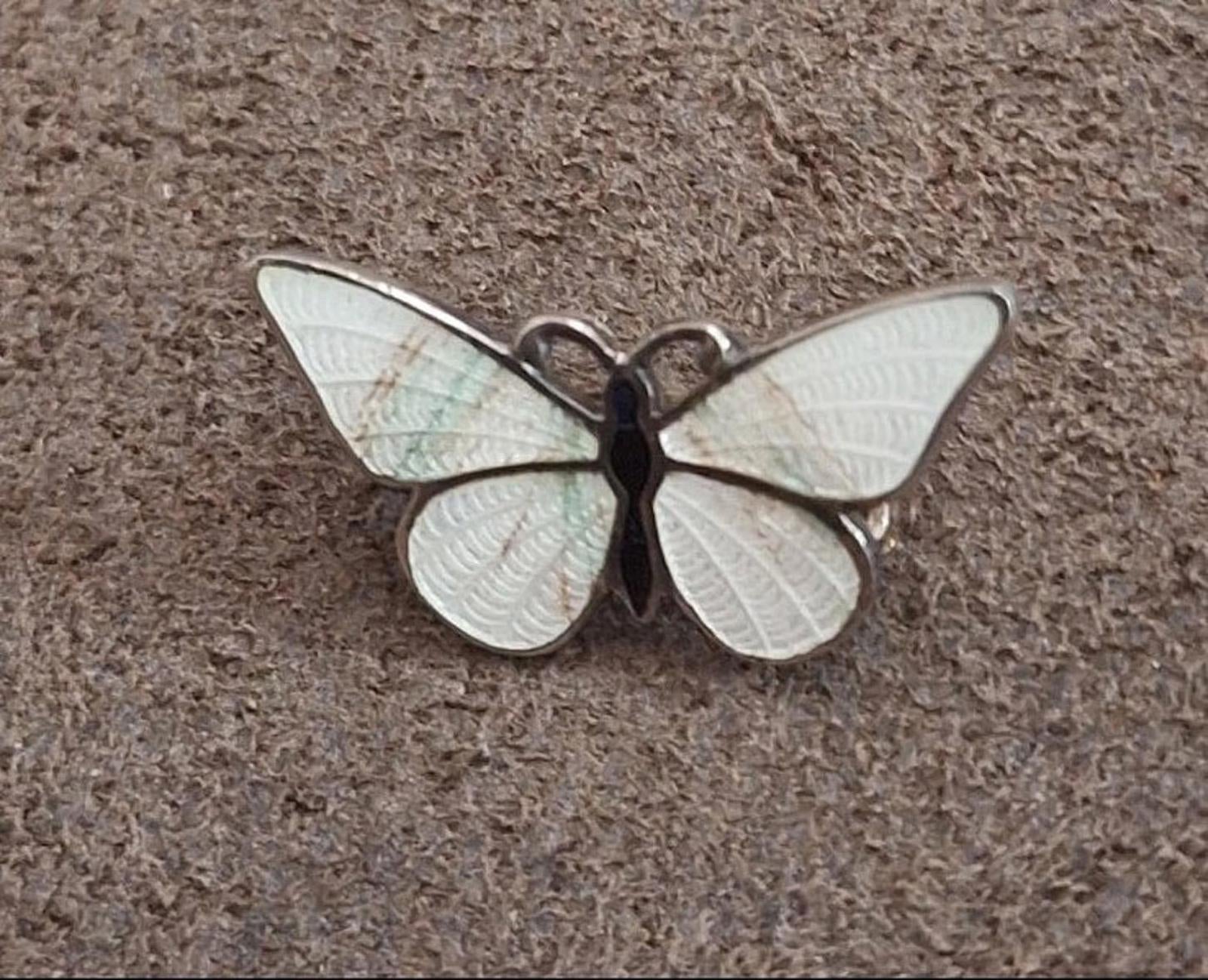 Enamel butterfly pin brooch with white textured wings and dark body on fabric.
