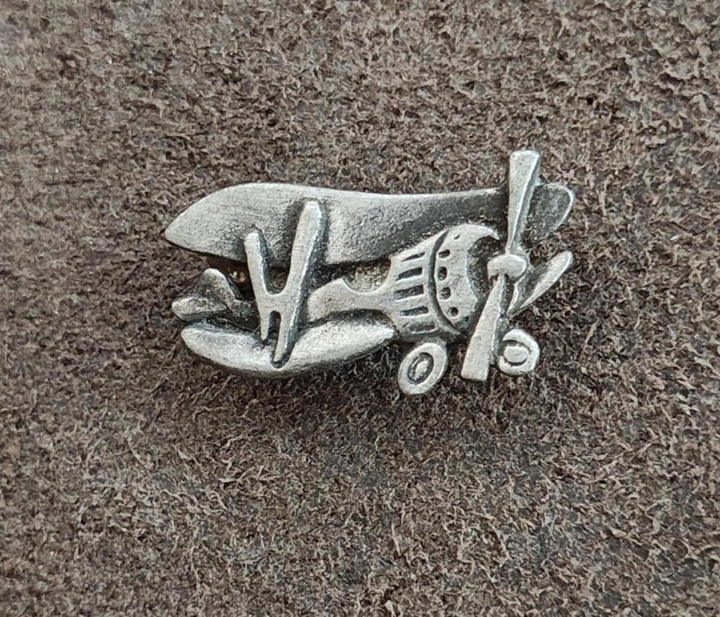 Pewter airplane brooch pin on textured surface, angled front view with propeller.