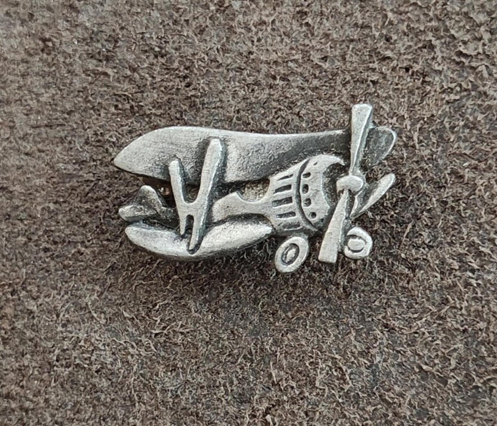 Pewter airplane brooch pin on textured surface, angled front view with propeller.