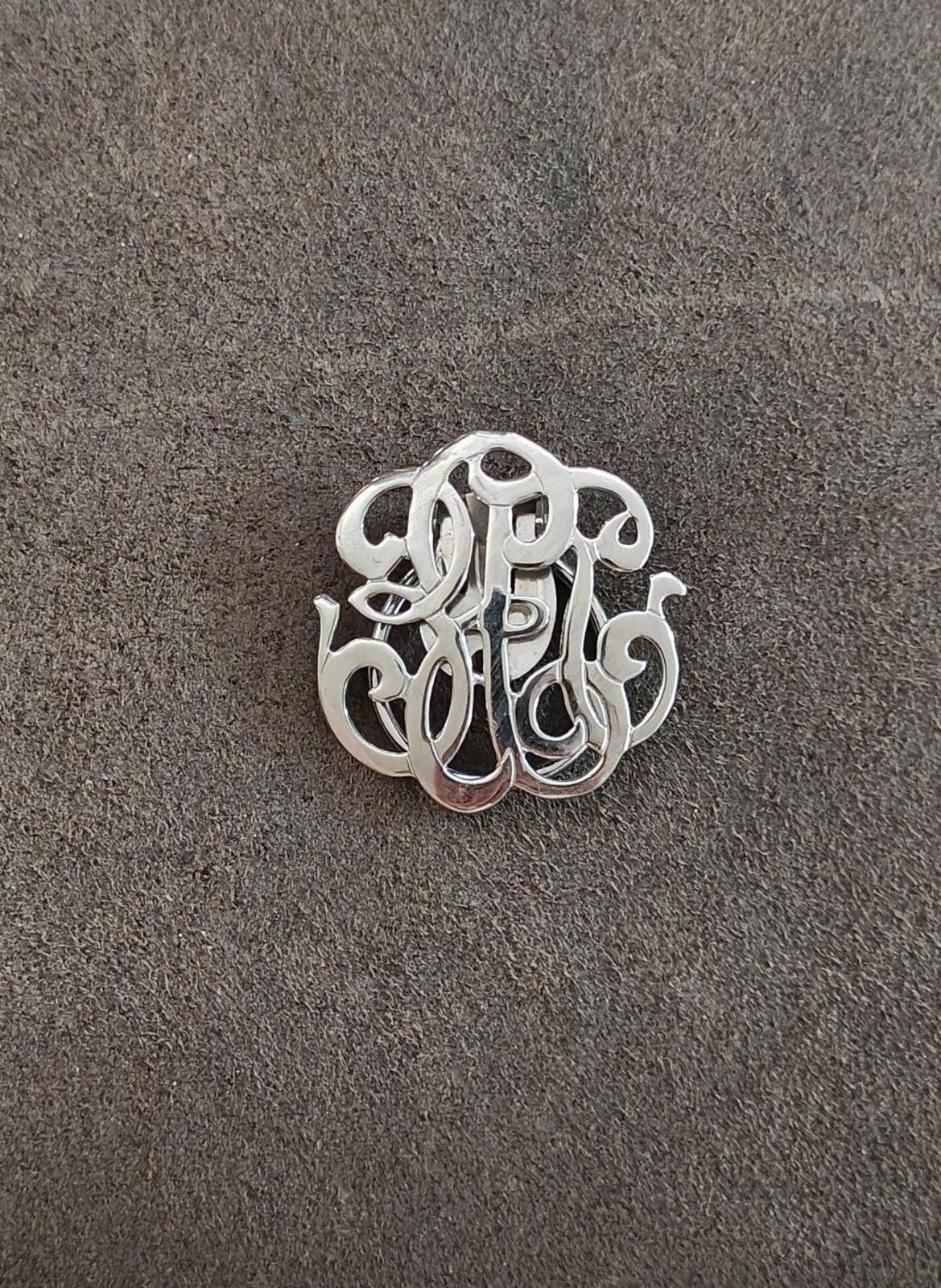 Silver-tone monogram scarf clip, front view of ornate cutout letters