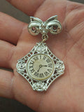 Silver-tone bow clock brooch with ornate square clock face, roman numerals, dangle.