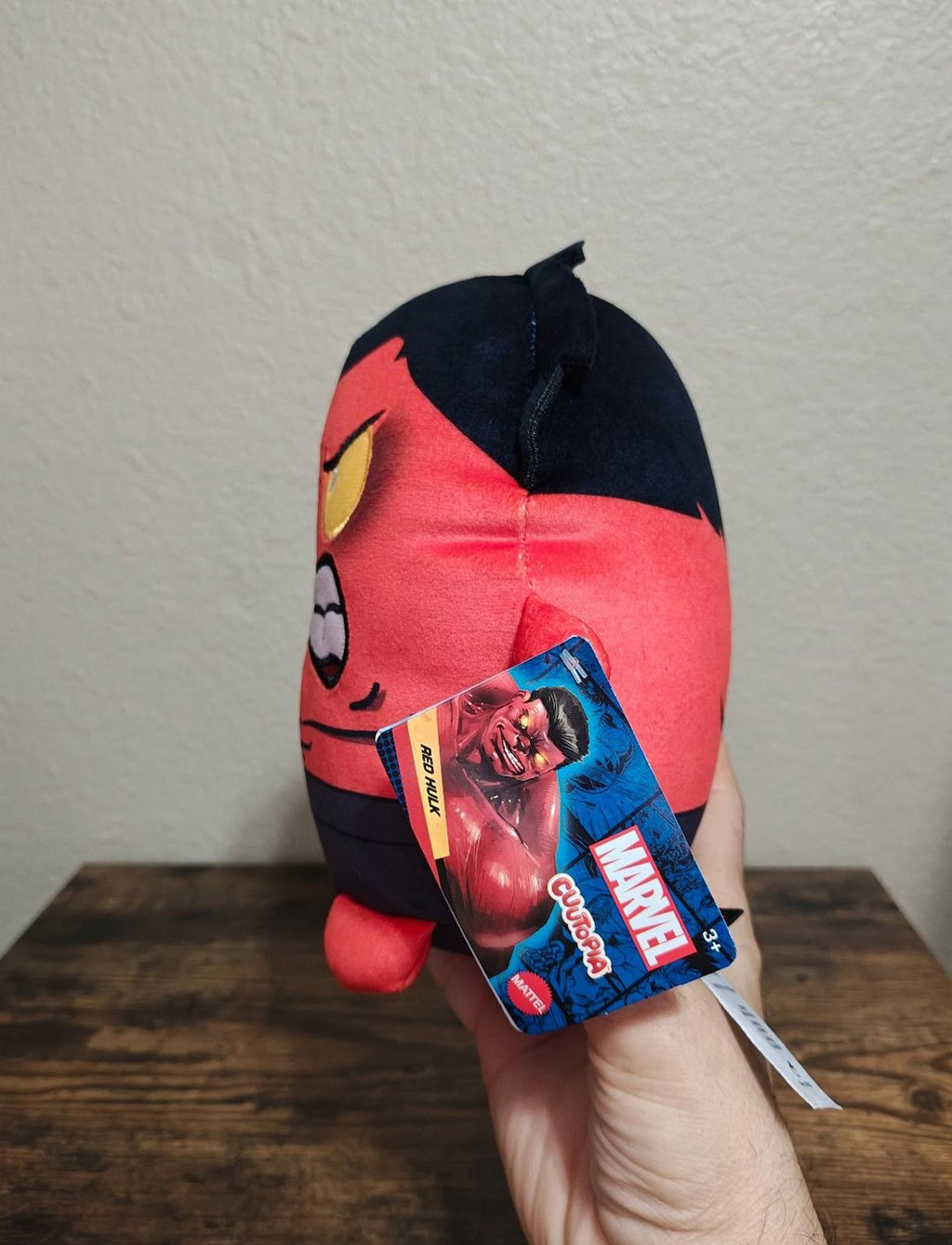 Side view red and navy plush character with attached blue hang tag