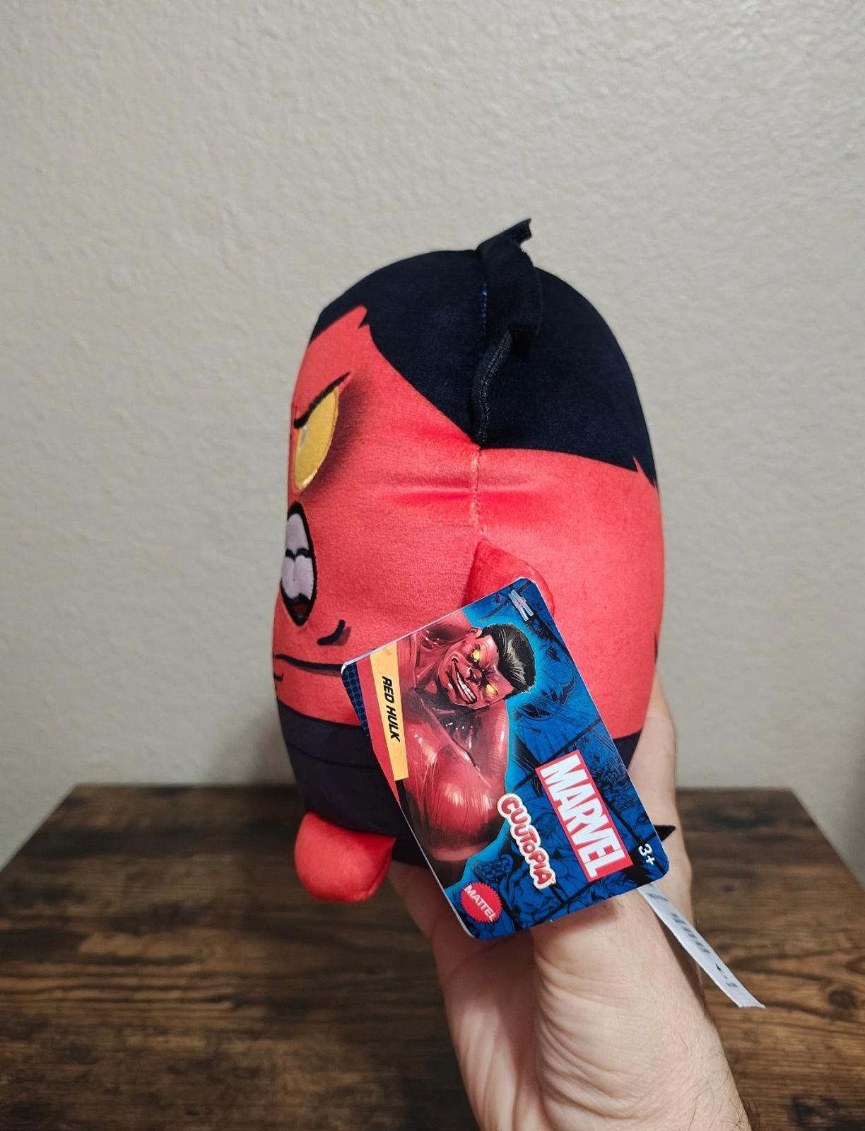 Side view red and navy plush character with attached blue hang tag
