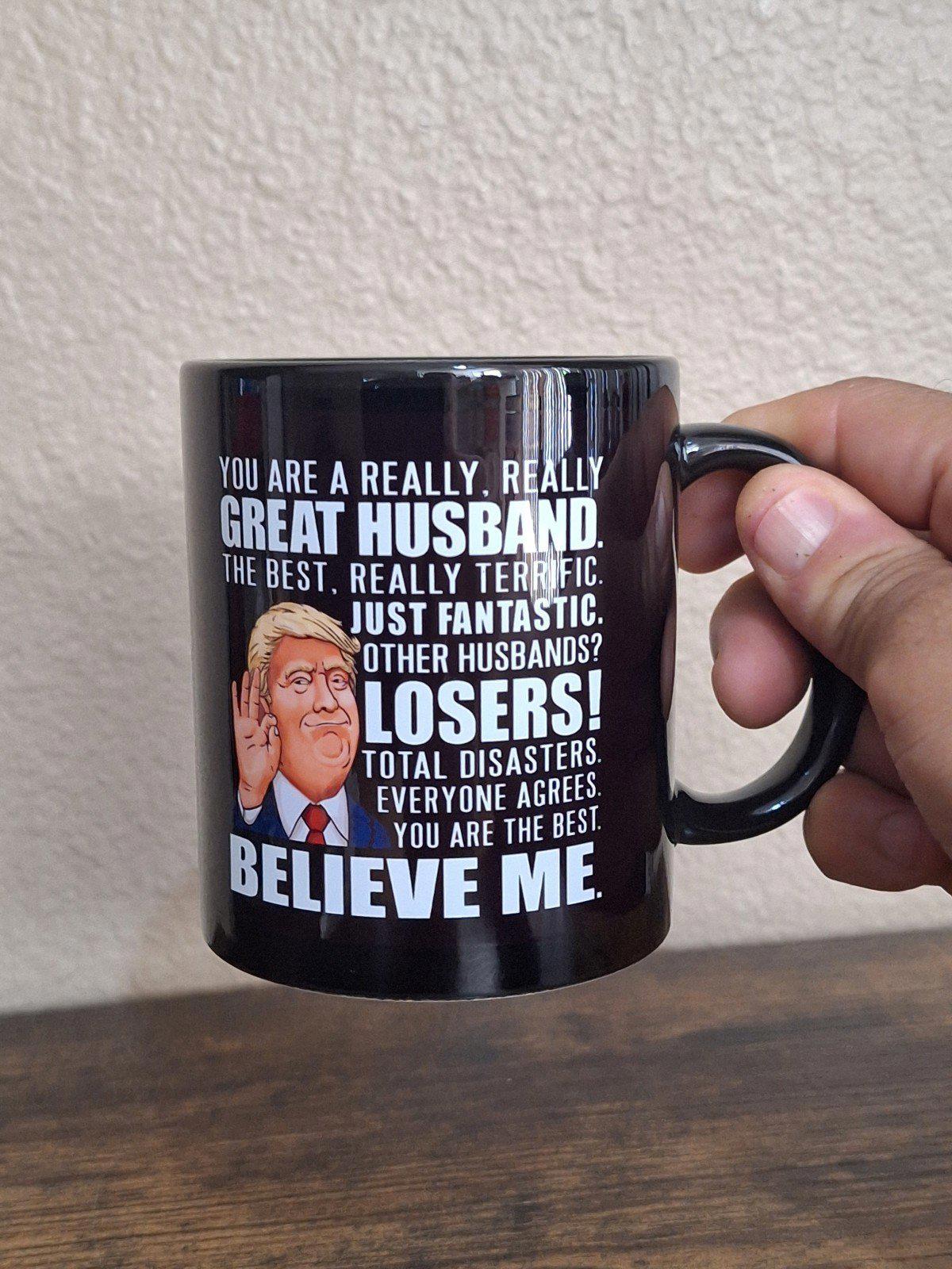 Black ceramic 11 oz mug showing "Great Husband" text and cartoon Donald Trump