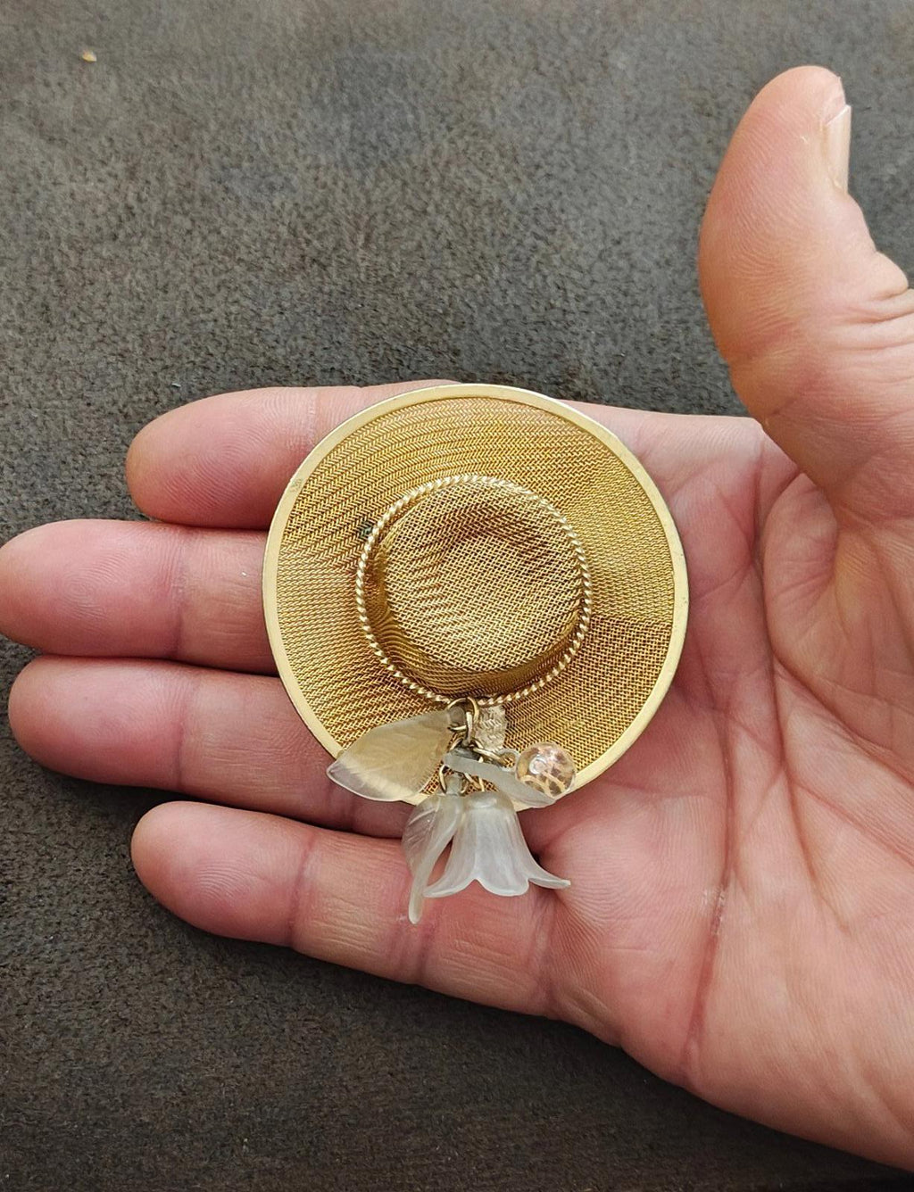 Gold-tone mesh sun hat brooch pin on hand showing inner ring and dangling white charm