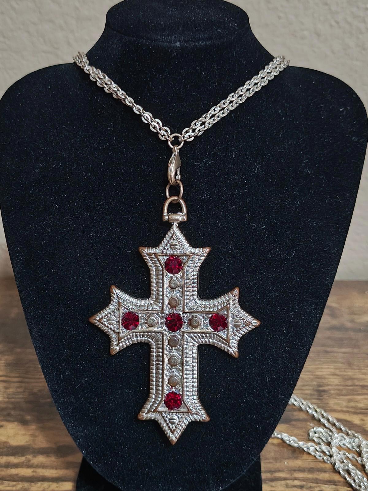 Silver tone cross pendant necklace with red rhinestones on a chain, worn on a bust