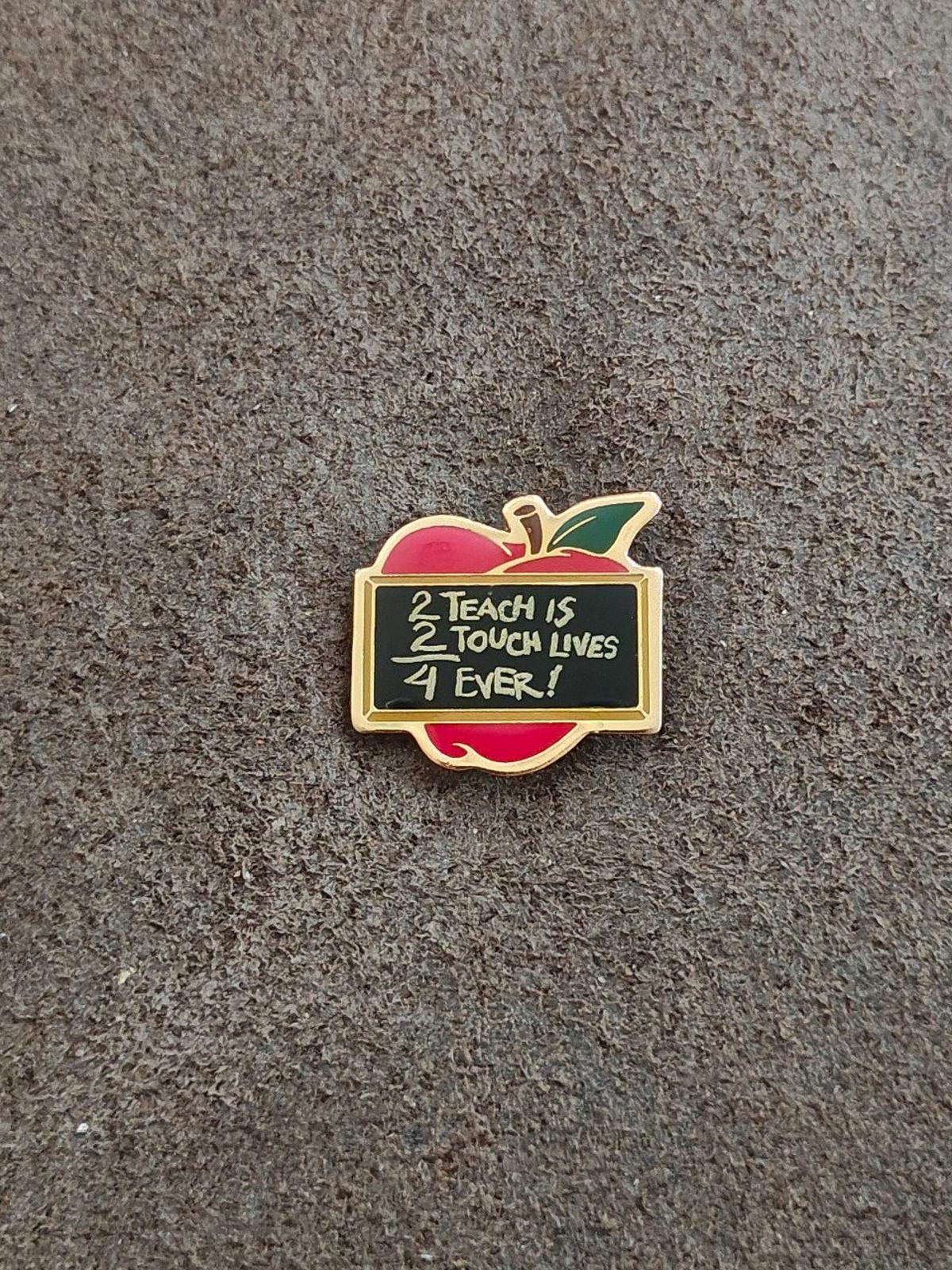 Gold-tone apple teacher pin with red and green enamel and black quote panel on gray background