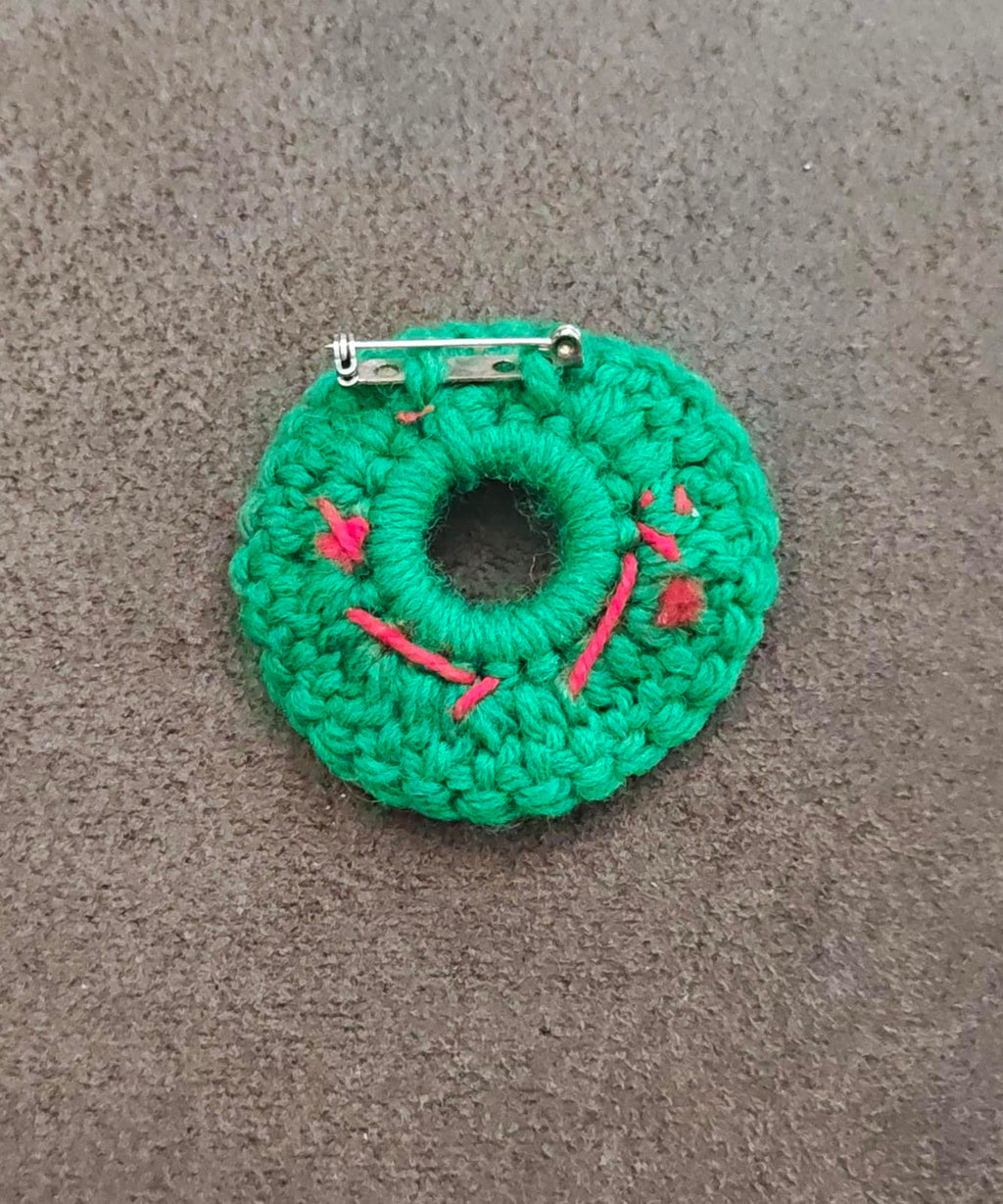 Green knitted wreath brooch with red berry accents and metal pin backing, front view